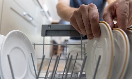 A man in front of an open dishwasher takes out clean dishes after washing.